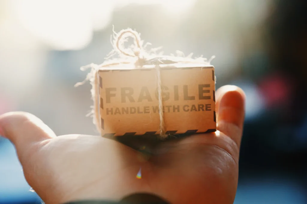 Hand holding a small parcel marked fragile, handle with care, for business courier delivery