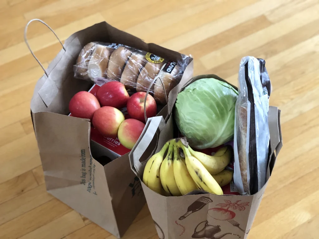 Paper grocery bags filled with fresh apples, bananas, lettuce and bread ready for delivery